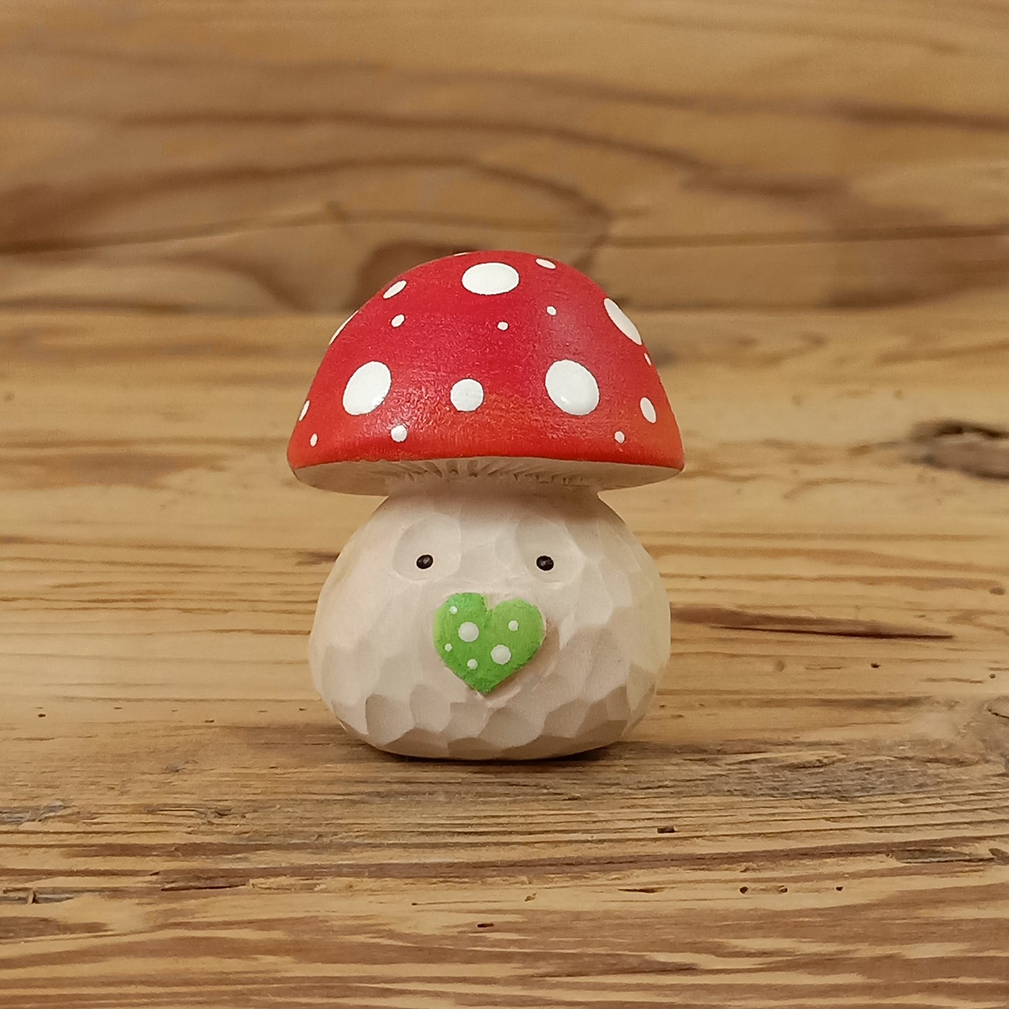 Glückspilz-Wichtel – liebevoll handgeschnitzte Holzfigur aus Lindenholz mit rotem Fliegenpilzhut, grüner Herznase und freundlichem Gesicht auf rustikalem Holzhintergrund. Handgefertigt von NaturWunderWerk.