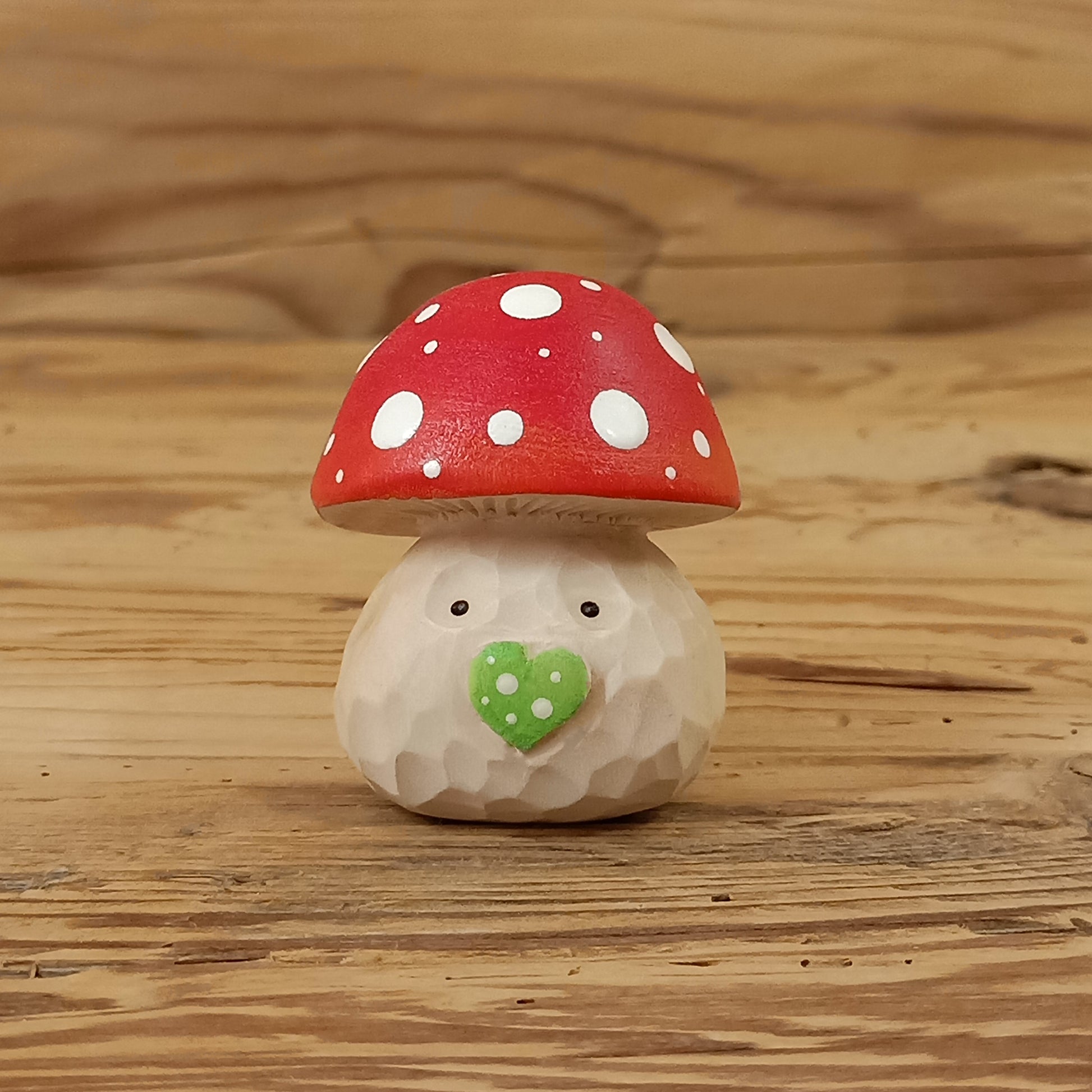 Glückspilz-Wichtel – liebevoll handgeschnitzte Holzfigur aus Lindenholz mit rotem Fliegenpilzhut, grüner Herznase und freundlichem Gesicht auf rustikalem Holzhintergrund. Handgefertigt von NaturWunderWerk.