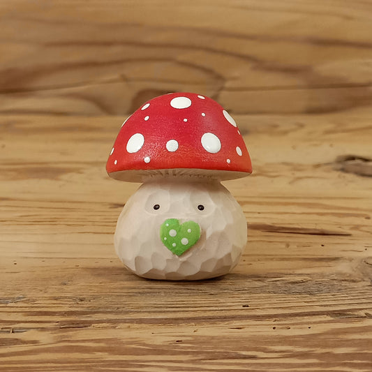 Glückspilz-Wichtel – liebevoll handgeschnitzte Holzfigur aus Lindenholz mit rotem Fliegenpilzhut, grüner Herznase und freundlichem Gesicht auf rustikalem Holzhintergrund. Handgefertigt von NaturWunderWerk.